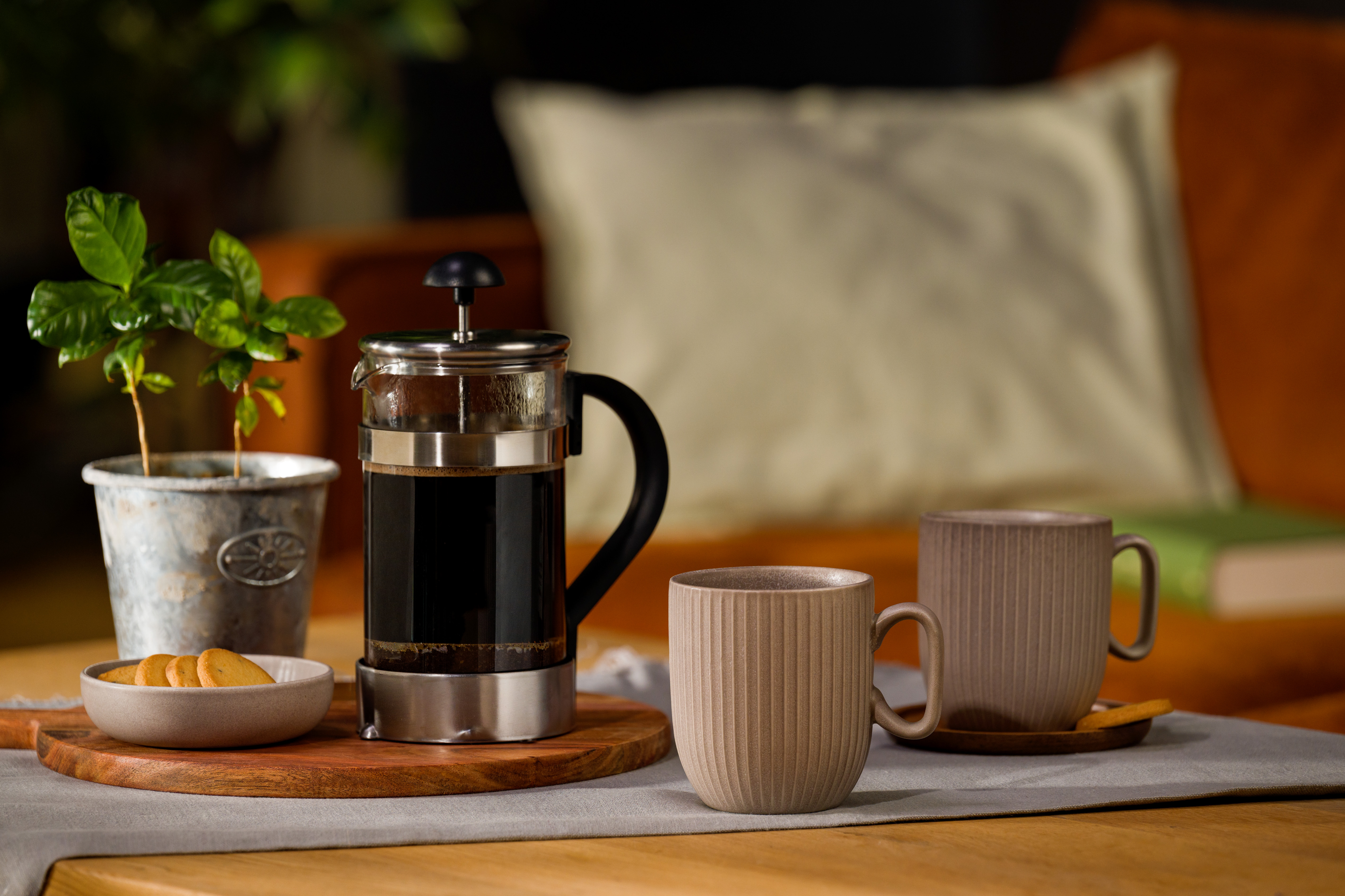 Gemütliche Kaffee-Stillife mit French-Press, zwei Keramiktassen, Minzepflanze und Keksschale auf Holztisch
