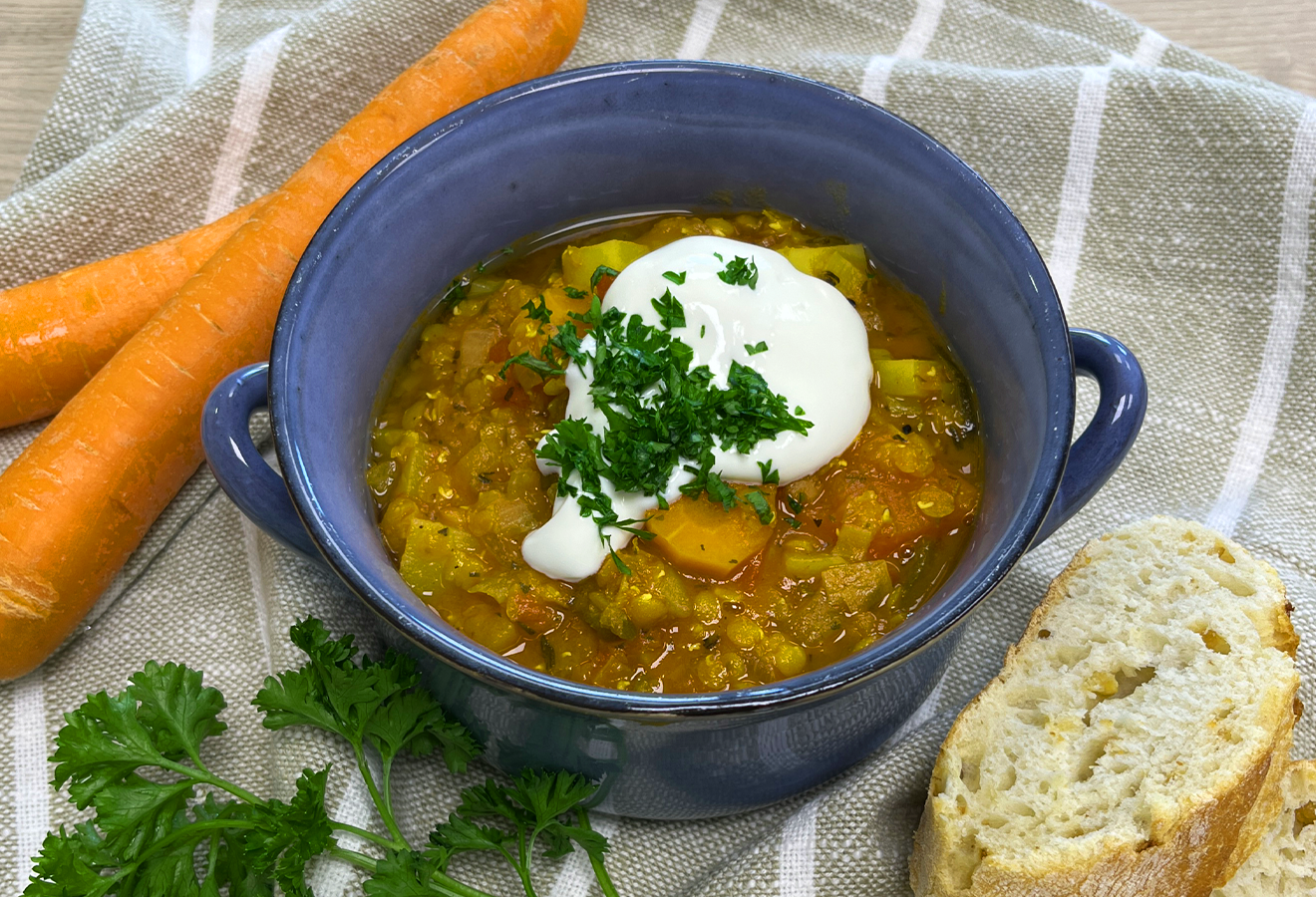 Vegetarischer Bauerntopf in blauer Schale mit Sauerrahm und Petersilie, serviert mit Möhre und Brot