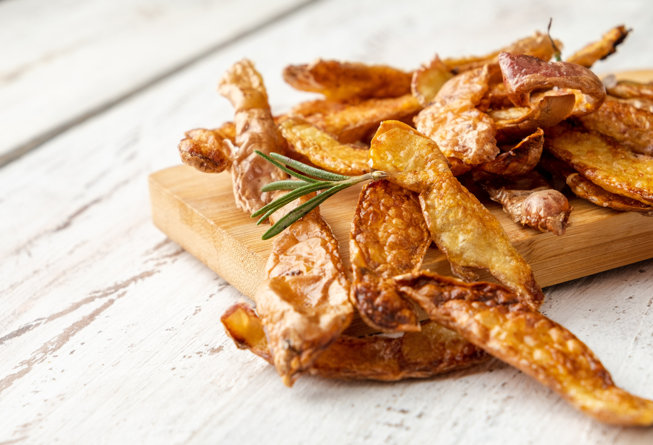 Knusprige goldbraune Kartoffelschalenchips auf Holzbrett, garniert mit Rosmarin, auf weißem Holzuntergrund.