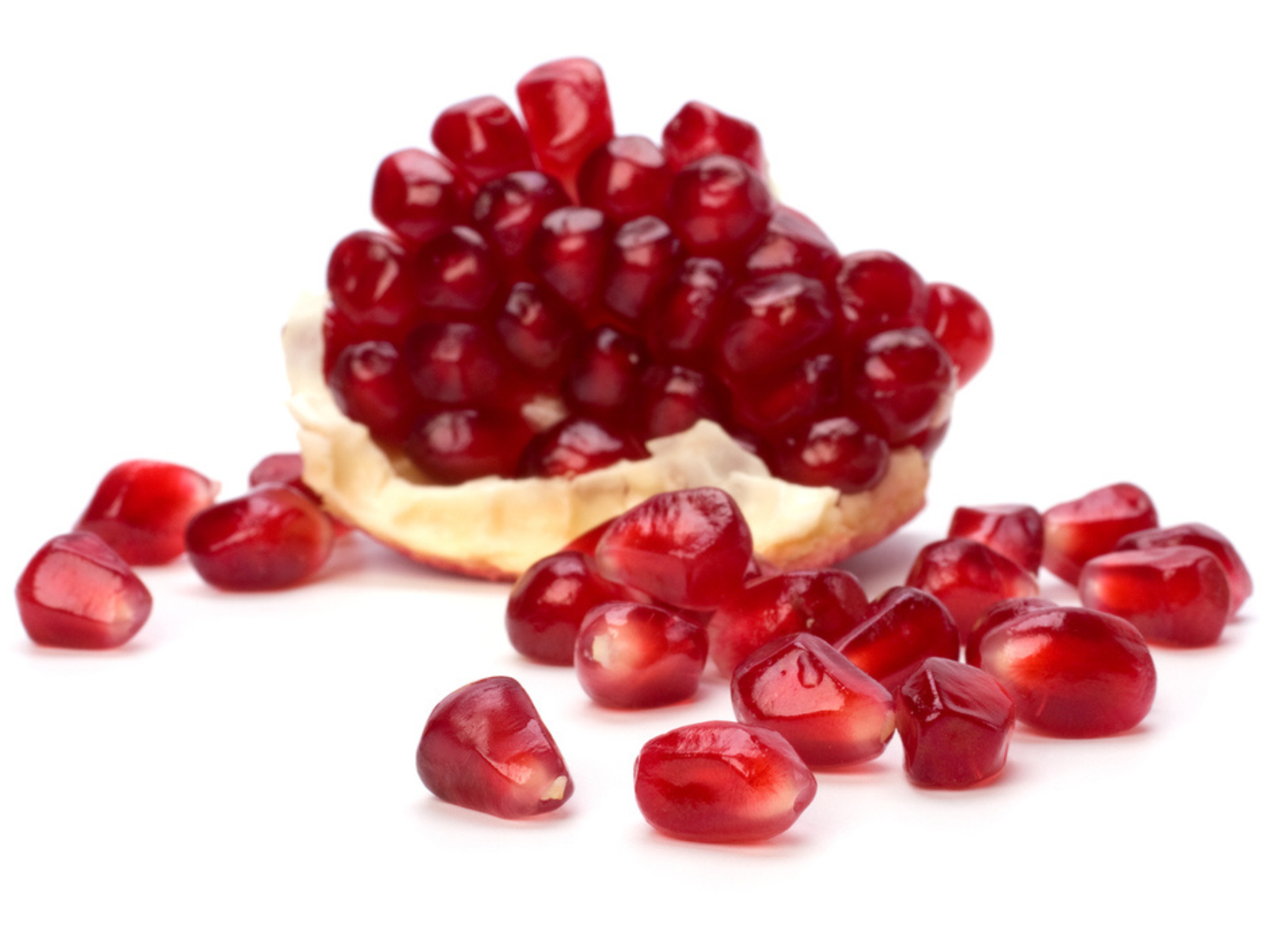 Rote Granatapfelkerne liegen auf einer weißen Oberfläche, einige noch in einem Stück der Fruchtschale
