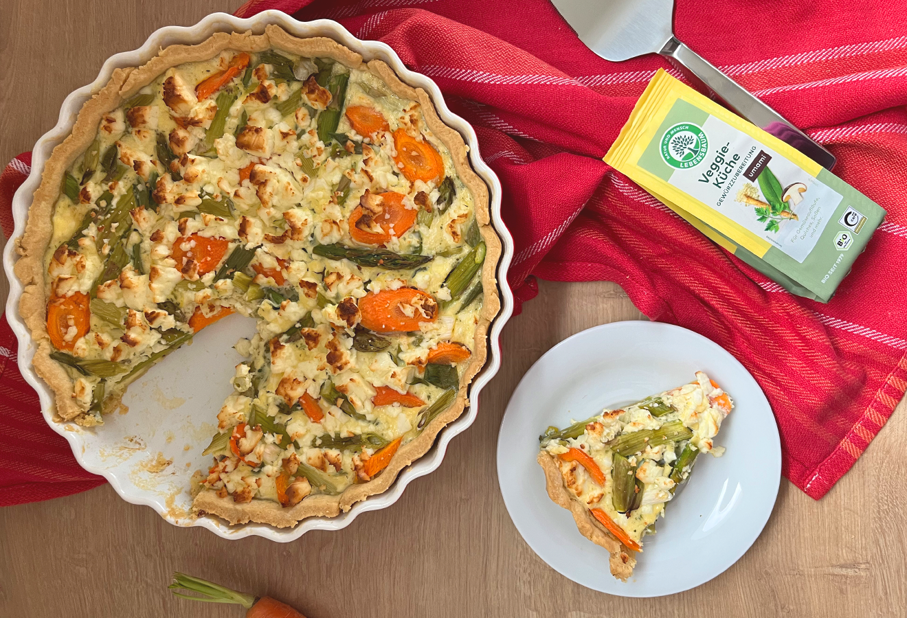 Gemüsequiche in einer Quicheform, daneben ein Teller mit einem Stück Quiche und eine Tüte LEBENSBAUM Veggie-Küche