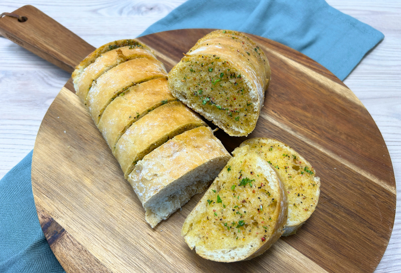 Kräuterbaguette mit grünen Kräutern und schwarzem Pfeffer, aufgeschnitten auf Holzbrett