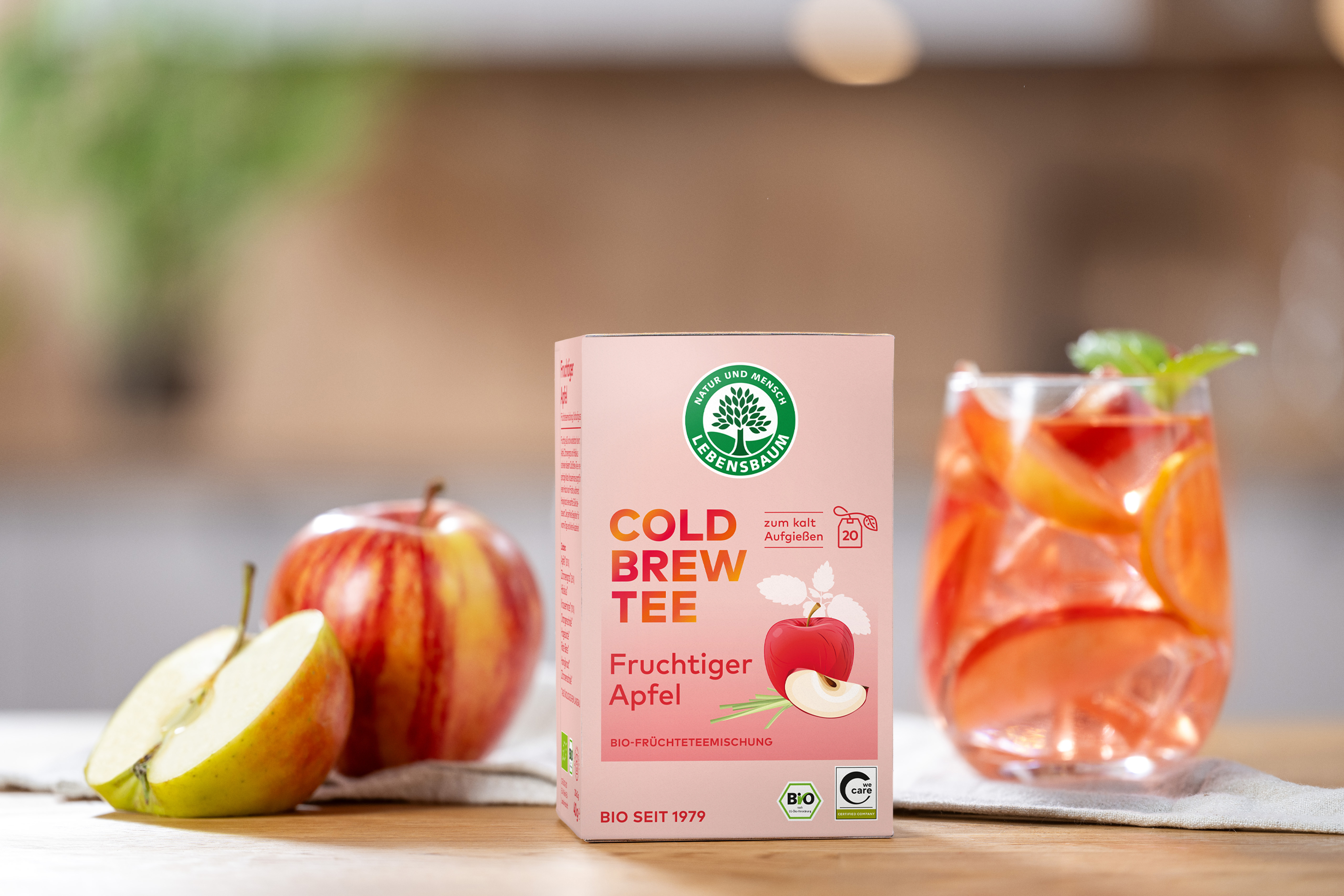 Cold Brew Verpackung steht auf einer Holzplatte. Daneben ist ein frischer Apfel und ein Glas mit kaltem Tee  