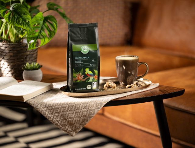 Herkunftskaffeepackung Guatemala, eine Tasse Kaffee und Gebäck auf einem Tisch in gemütlicher Wohnzimmeratmosphäre