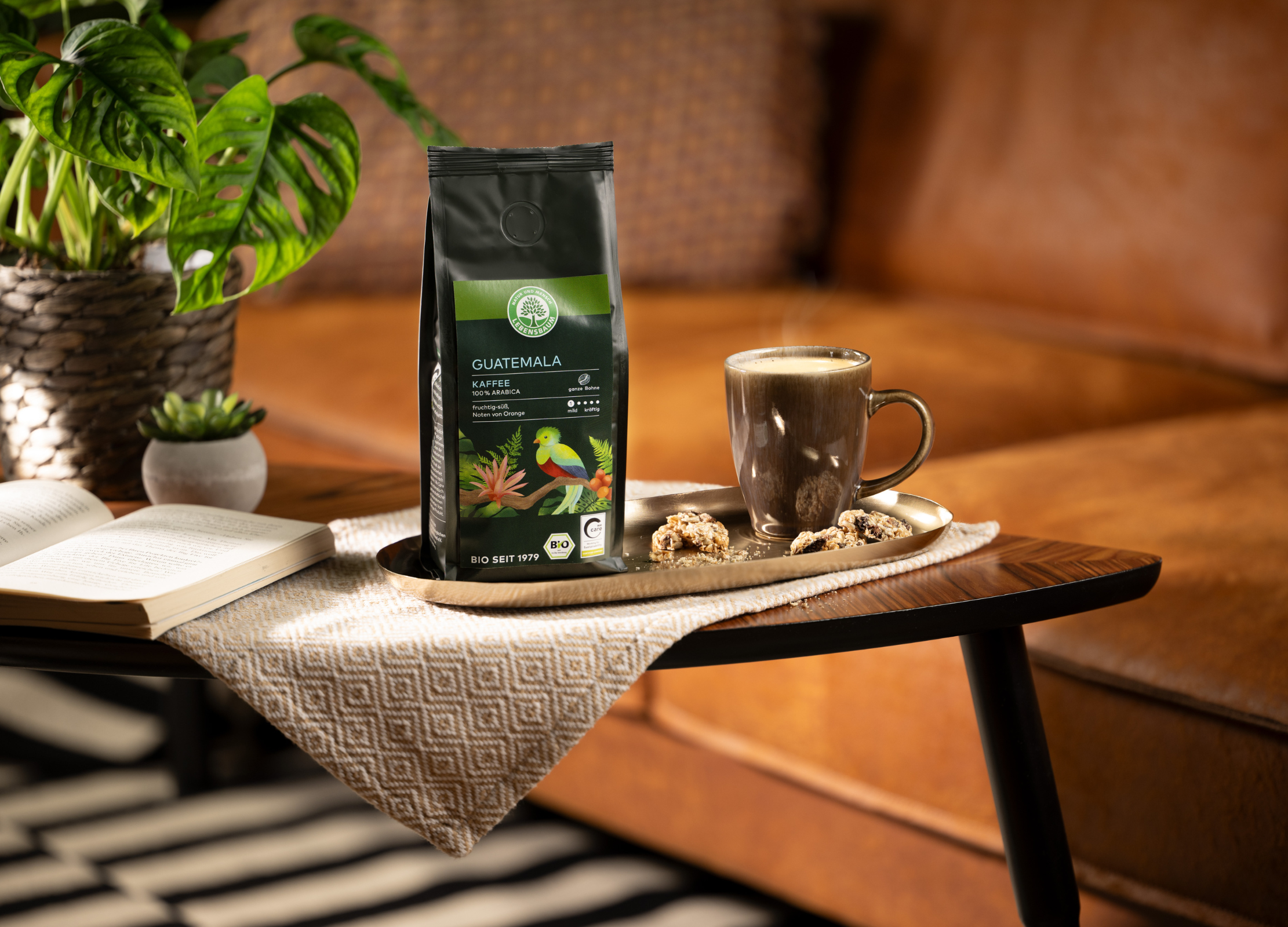 Herkunftskaffeepackung Guatemala, eine Tasse Kaffee und Gebäck auf einem Tisch in gemütlicher Wohnzimmeratmosphäre