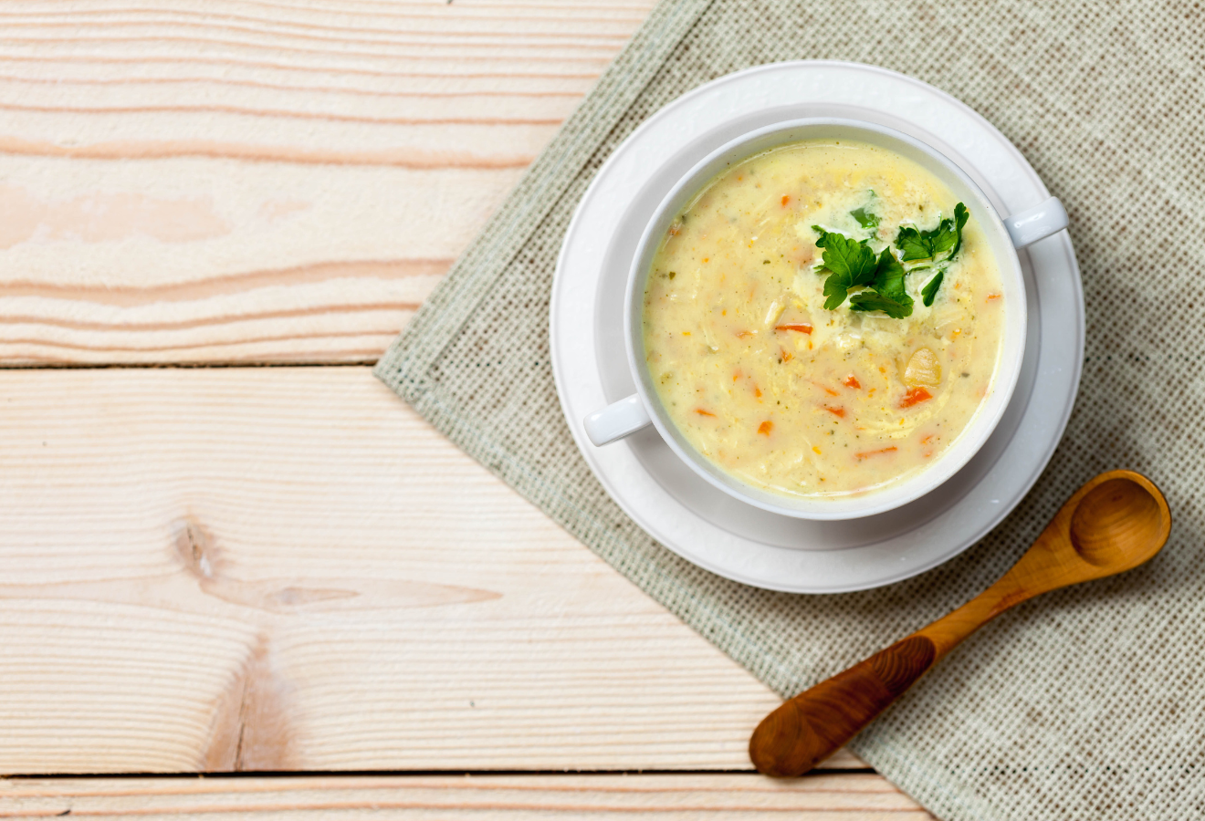 Thai-Suppe in einer weißen Schale, daneben ein Holzlöffel