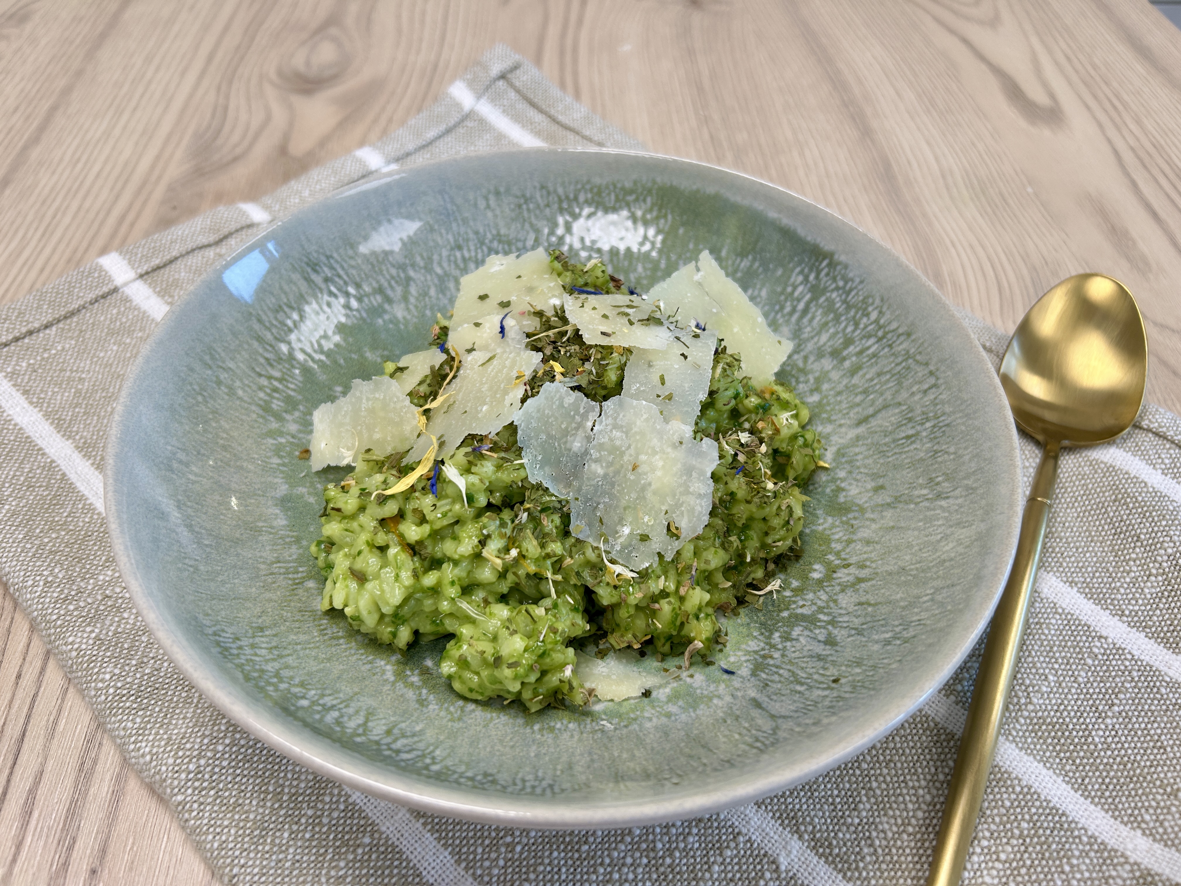 Grünes Risotto mit Kräutern und Parmesanspänen in graugrüner Schale, garniert mit frischen Kräutern.
