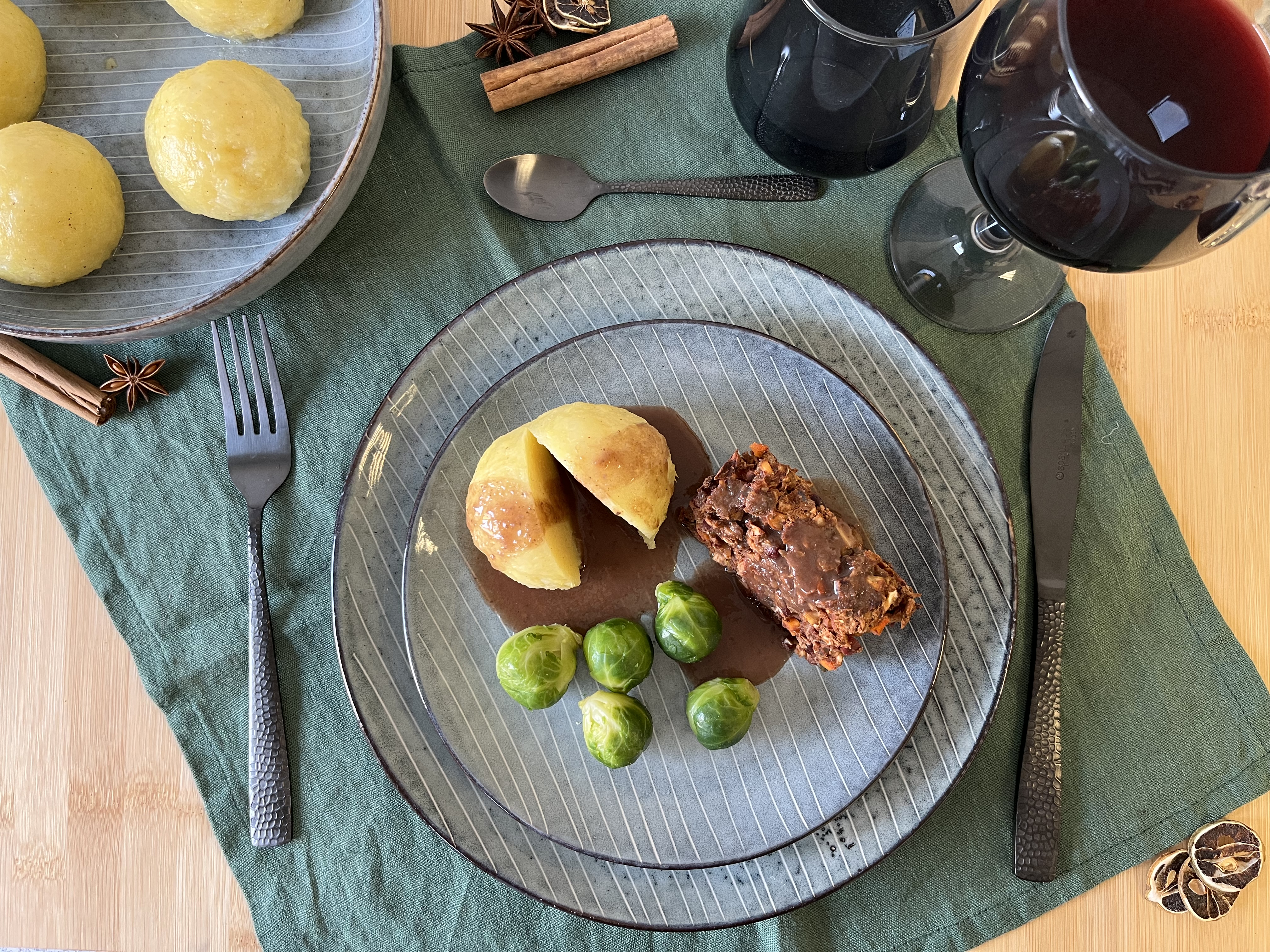 Elegant angerichteter Nussbraten mit Kartoffeln, Rosenkohl und Rotwein-Sauce auf grauem Teller, festlich gedeckter Tisch mit Sternanis und Zimt.