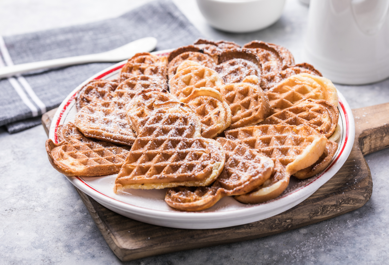  Wintergewürz-Waffeln auf einem weißen Teller auf einem Holzbrett mit Puderzucker garniert