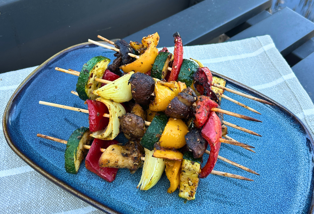 Gegrillte Gemüsespieße mit buntem Gemüse wie Paprika, Zucchini und Pilzen auf blauem Teller, mit Gewürzbelag.