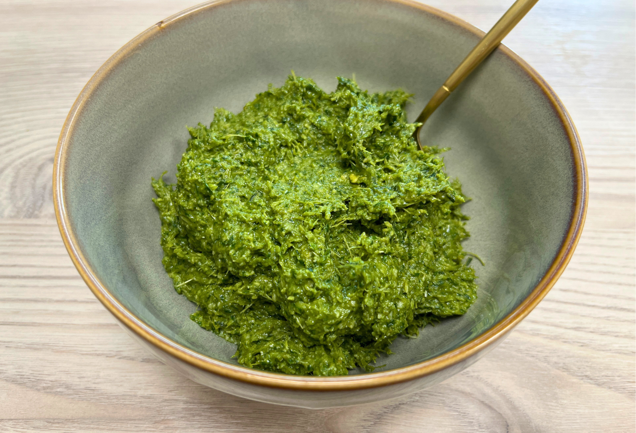 Karottengrün-Pesto in graugrüner Schale mit Messingrand und Holzlöffel auf Holztisch