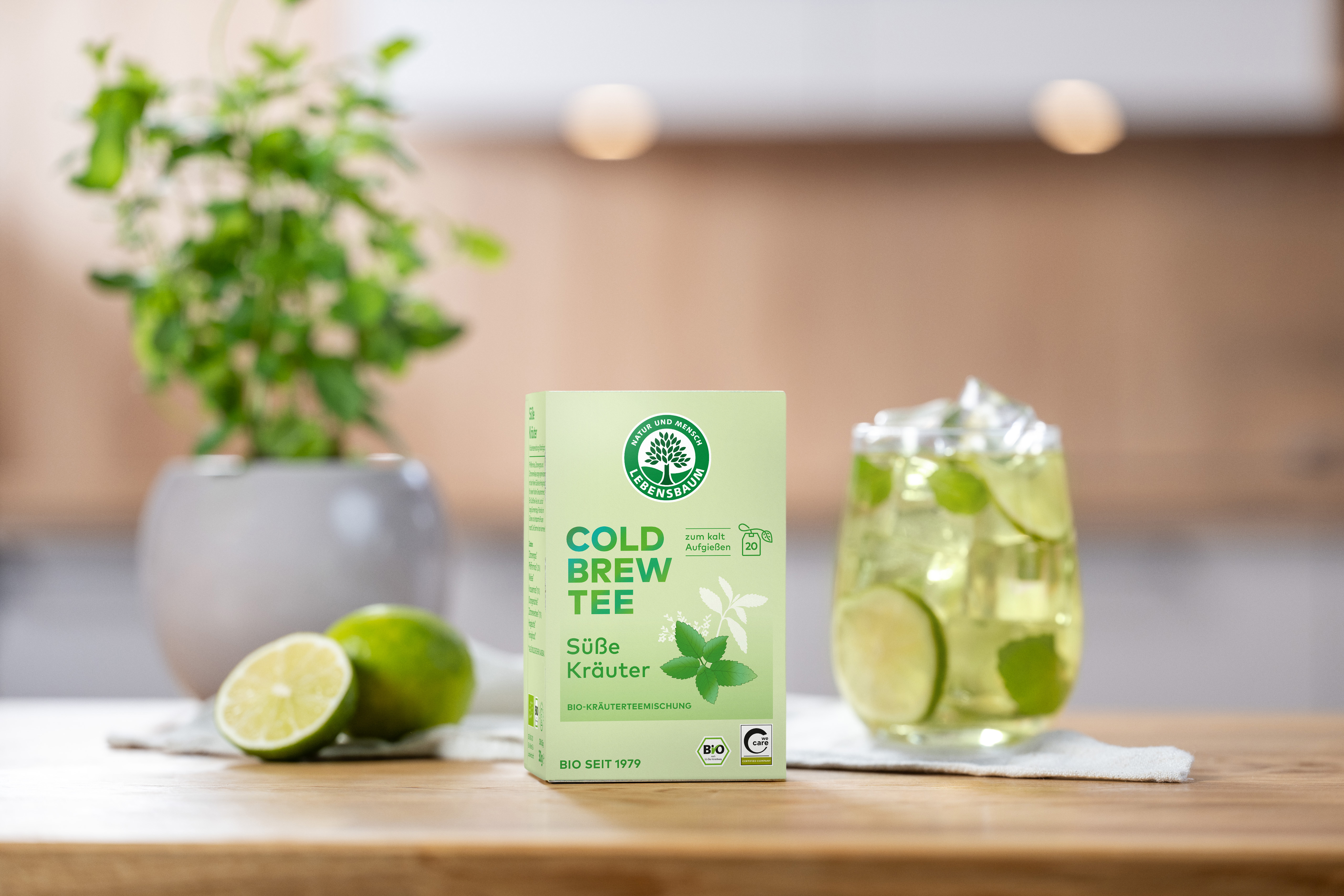 Cold Brew Verpackung steht auf einer Holzplatte. Daneben ist eine halbierte Limette und ein Glas mit kaltem Tee  