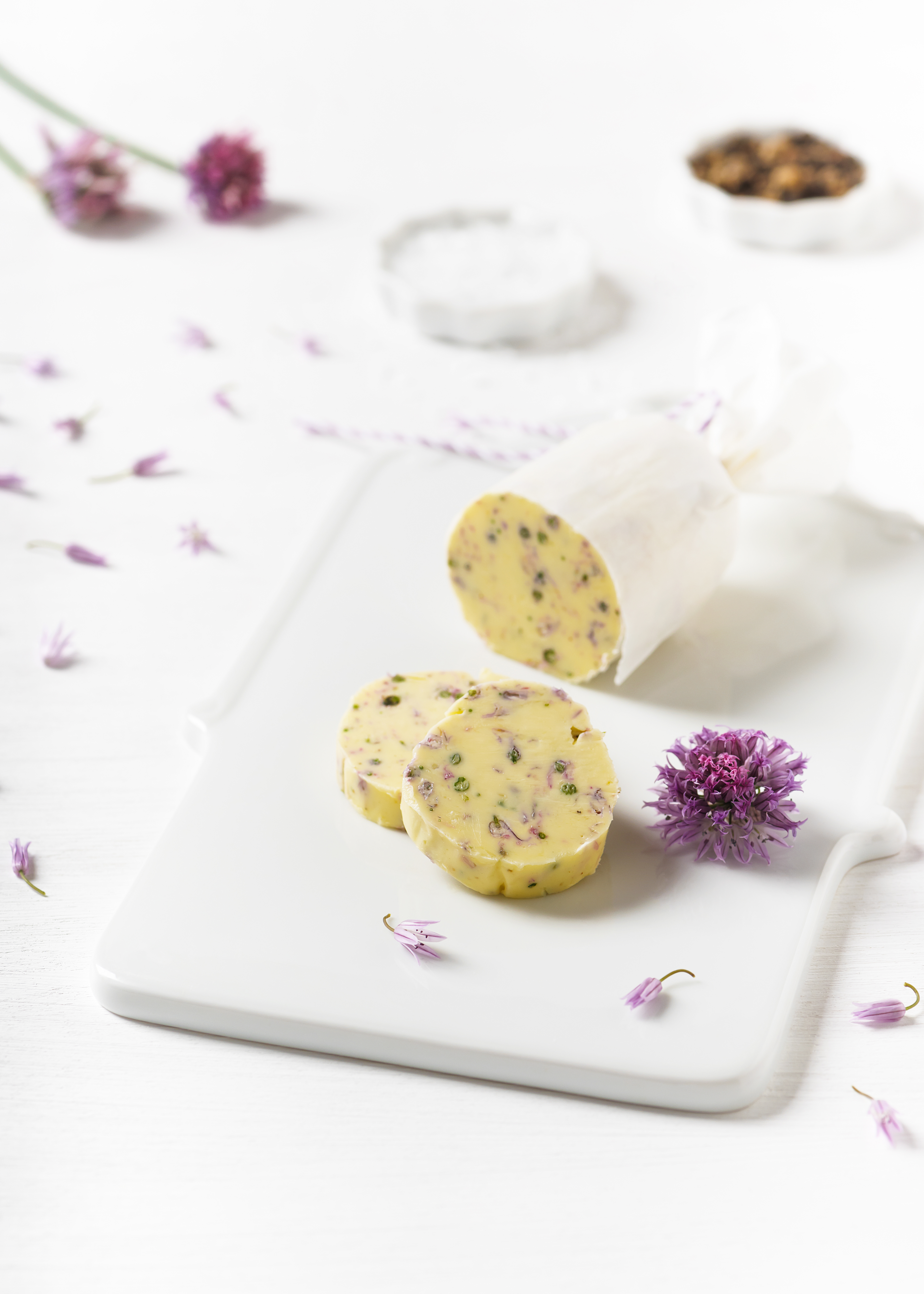 Blütenbutter mit Kräutern und getrockneten Blüten, auf weißem Teller mit frischen Blüten arrangiert