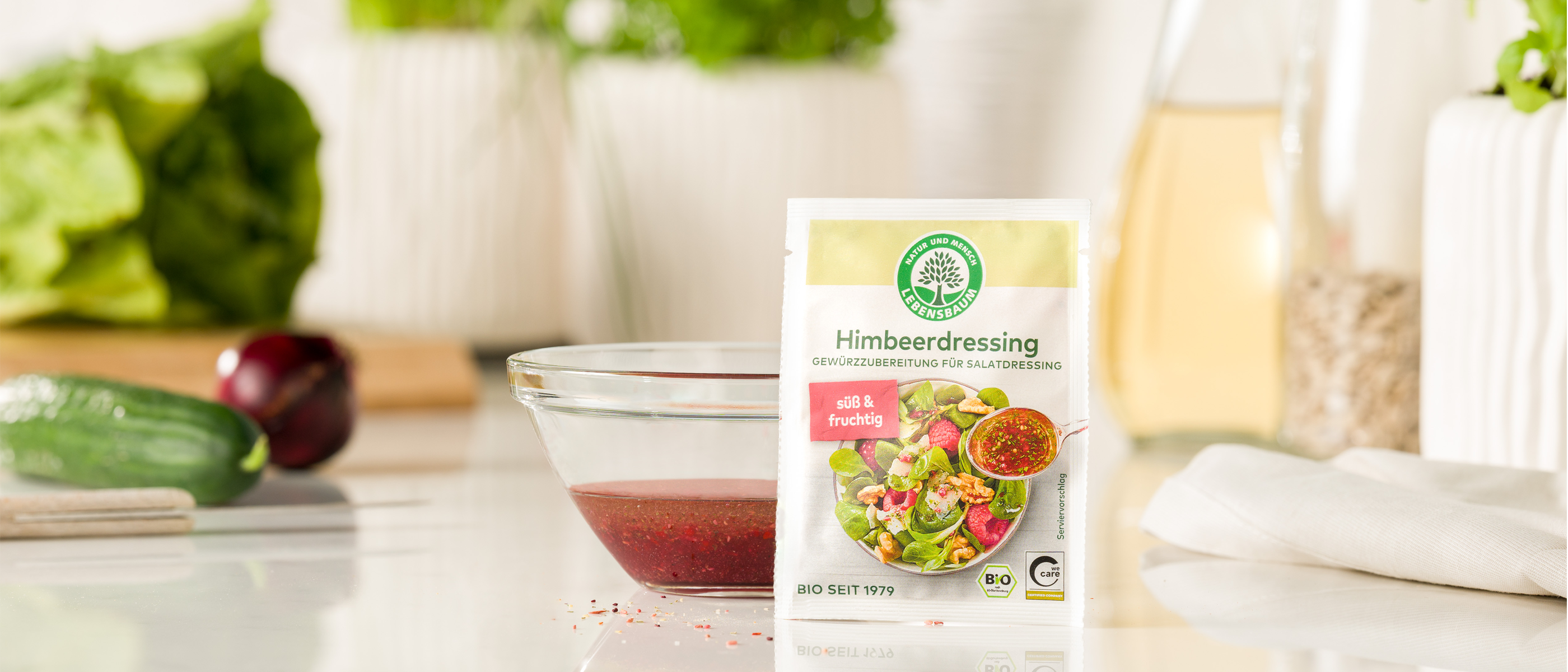 Eine Tüte Lebensbaum Himbeerdressing steht auf einer Küchenarbeitsplatte neben einer Glasschüssel mit angerührtem Dressing