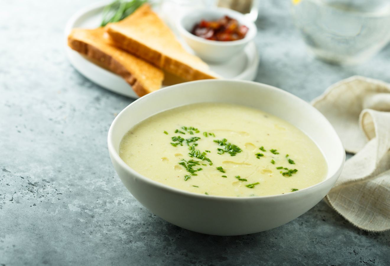 Exotische Kartoffelsuppe in einer weißen Schüssel mit Petersilie garniert, im Hintergrund Brotscheiben