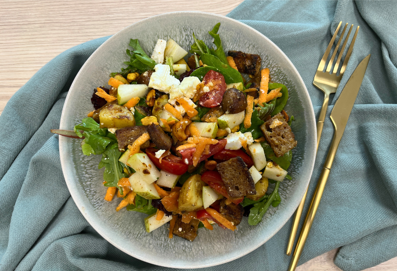 Herbstlicher Brotsalat mit knusprigen Brotwürfeln, Rucola, Karotten, Kartoffeln, Roten Rüben und Käse in grauer Schale