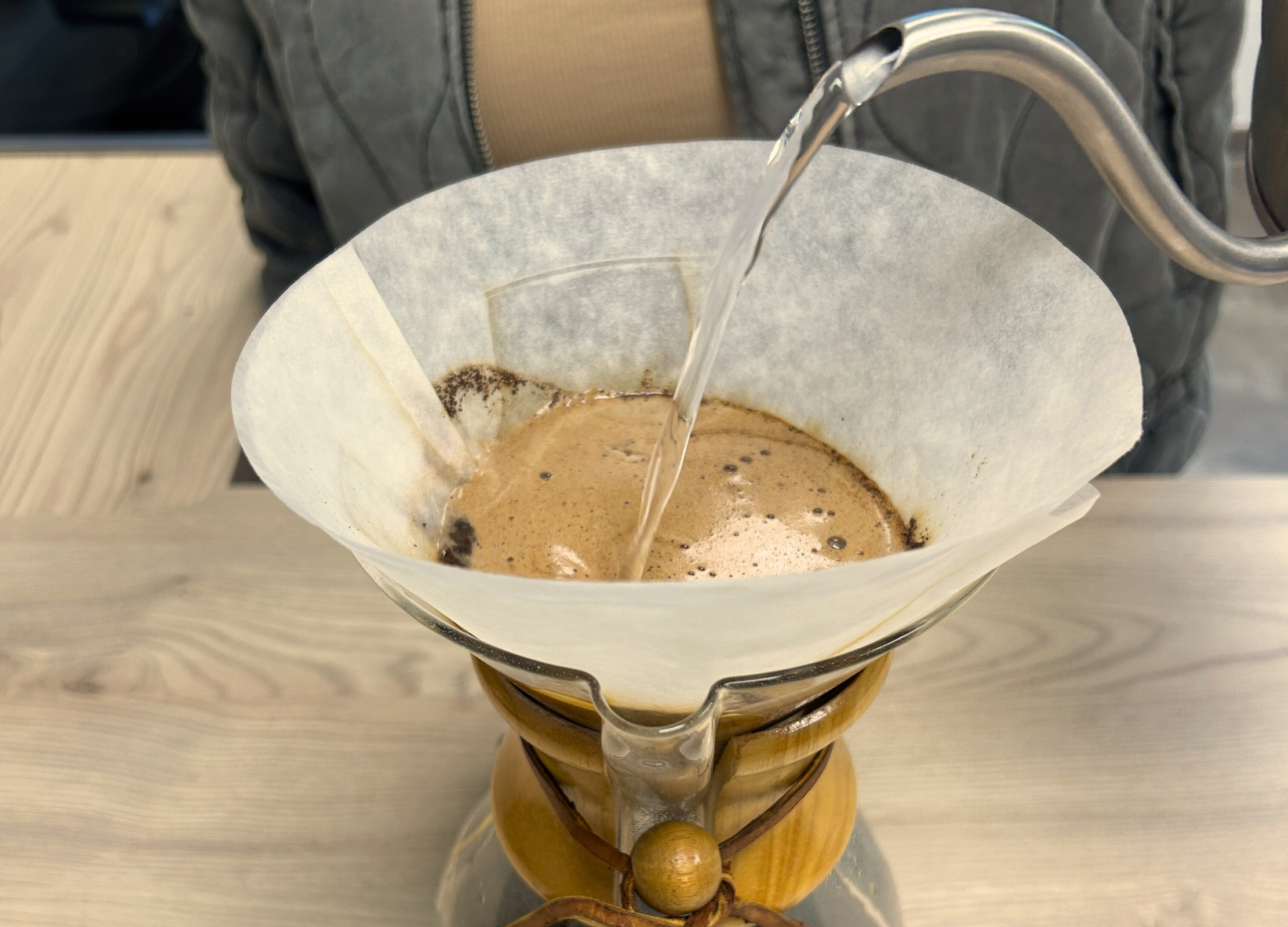 Heißes Wasser wird langsam in kreisenden Bewegungen auf das Kaffeepulver im Filter einer Chemex-Karaffe gegossen