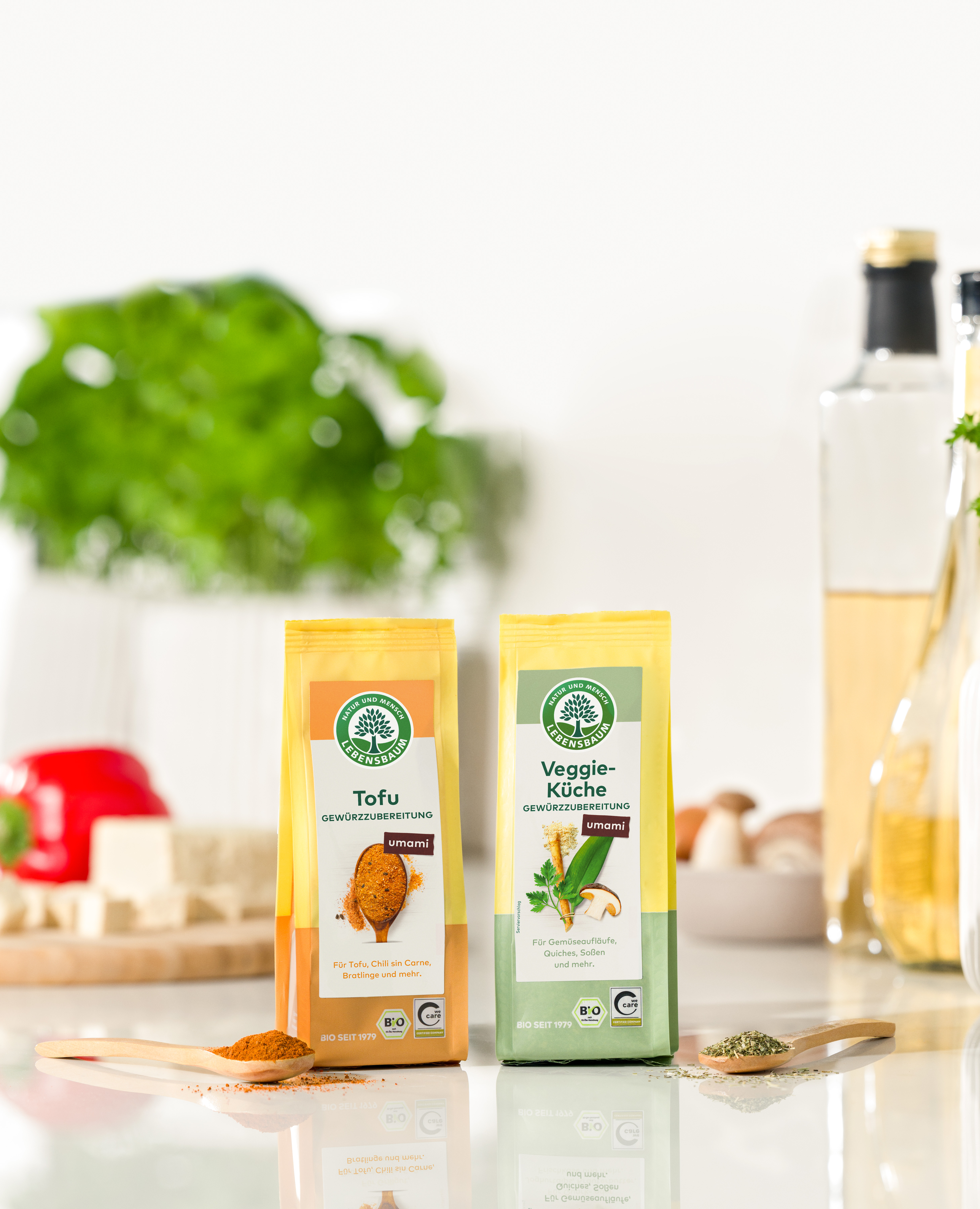 Zwei Bio-Gewürzmischungen in gelben Papierbeuteln: Tofu-Gewürzzubereitung mit orange-rotem Design und Veggie-Küche mit grünem Design, umami-Geschmack, mit Holzlöffeln und Gewürzen in Küchen-Lifestyle-Szenerie.