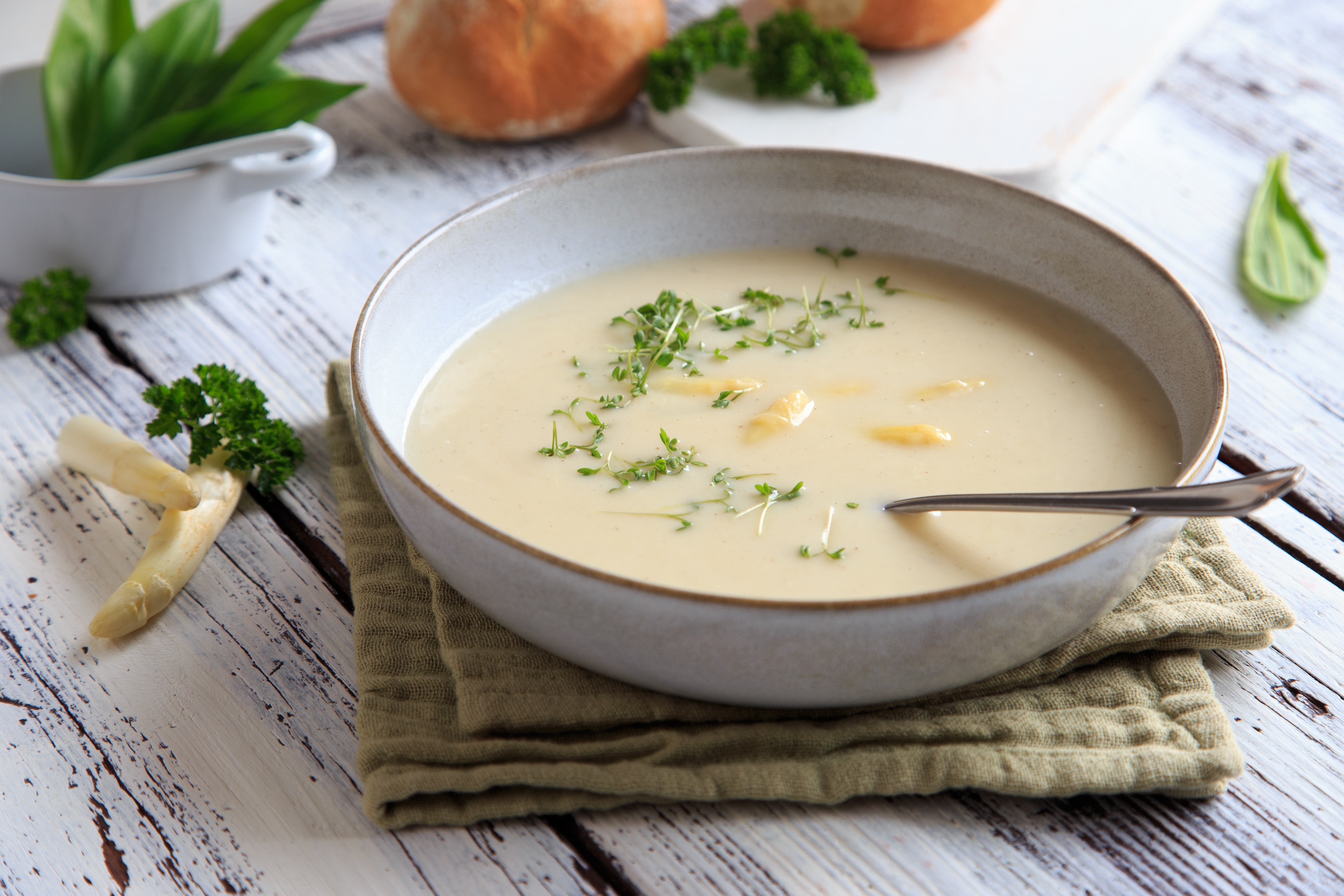 Cremige Suppe mit Lauch und Gewürzen in weißer Schale, garniert mit Sauerrahm und schwarzem Pfeffer