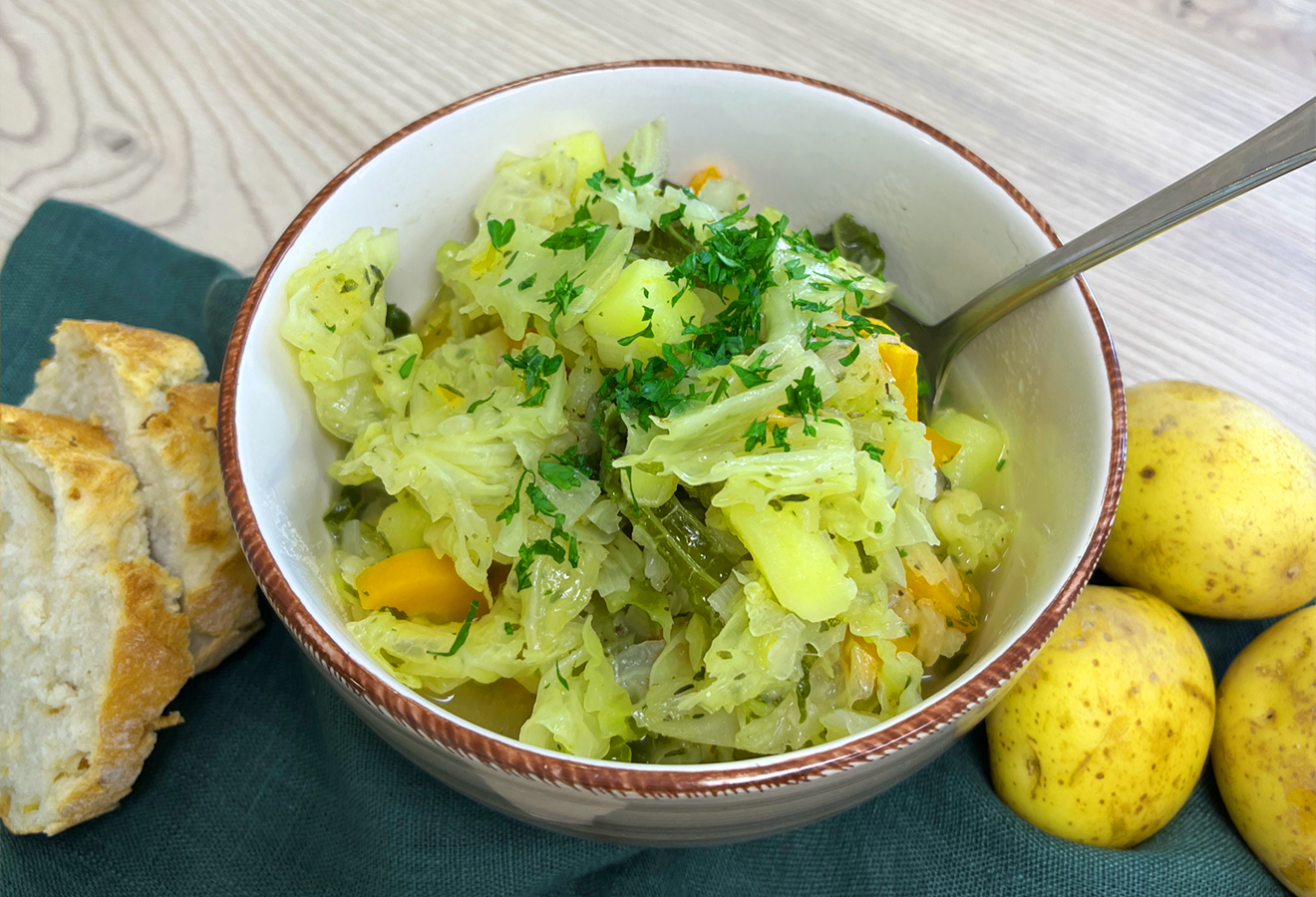 Wirsingeintopf in Schüssel mit Kartoffeln, Brokkoli und frischen Kräutern, serviert mit Brot und Kartoffeln.