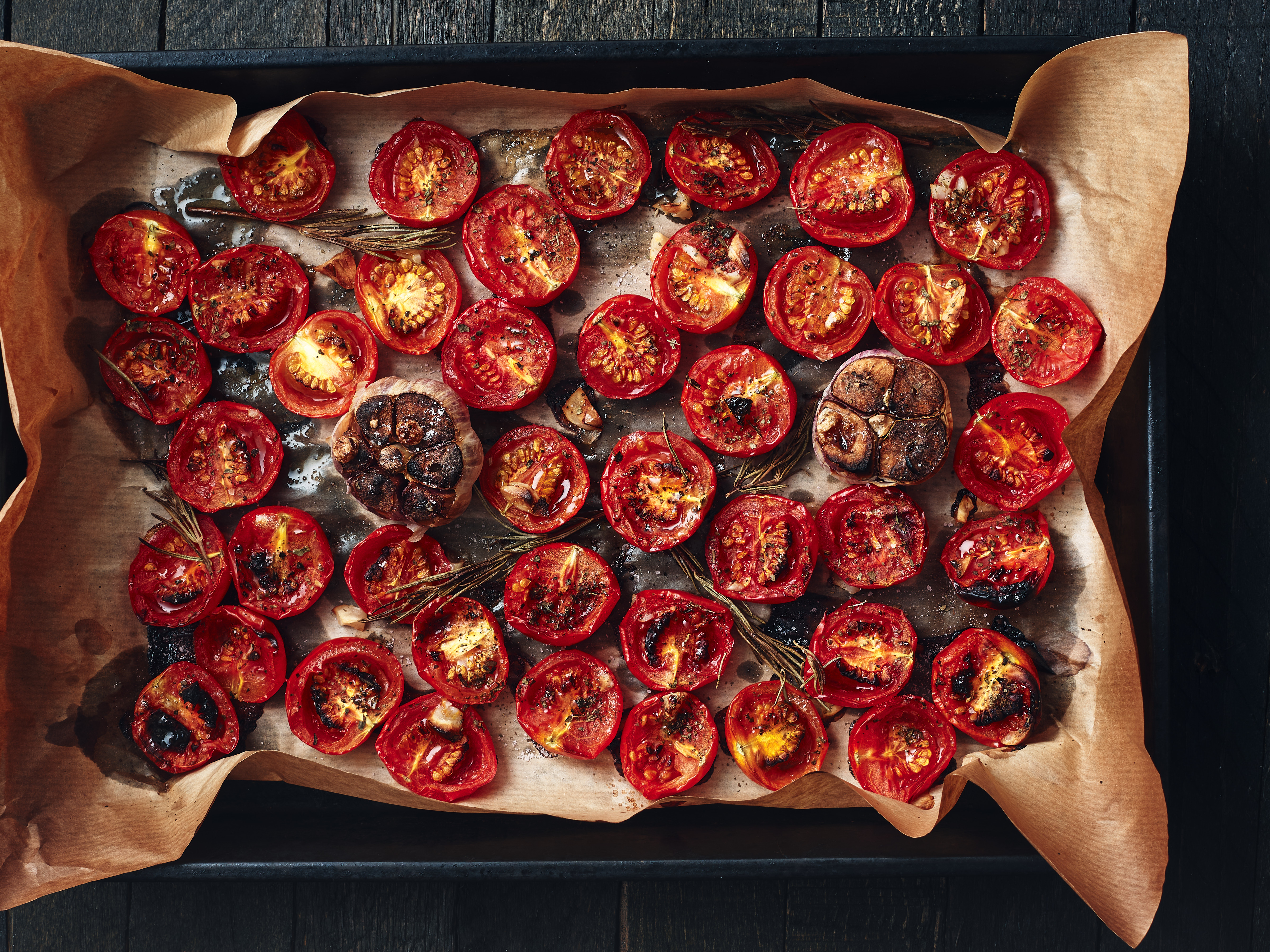 Getrocknete Tomatenscheiben und karamellisierte Zwiebeln auf Backpapier, garniert mit Rosmarinzweigen.