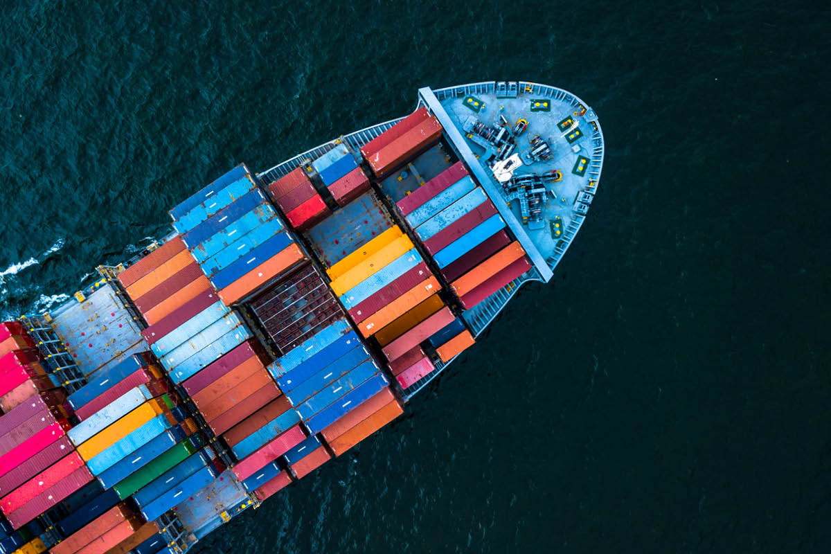 Luftaufnahme eines Containerschiffs mit farbigen Frachtkontainern auf dunkelblauen Ozeanwellen