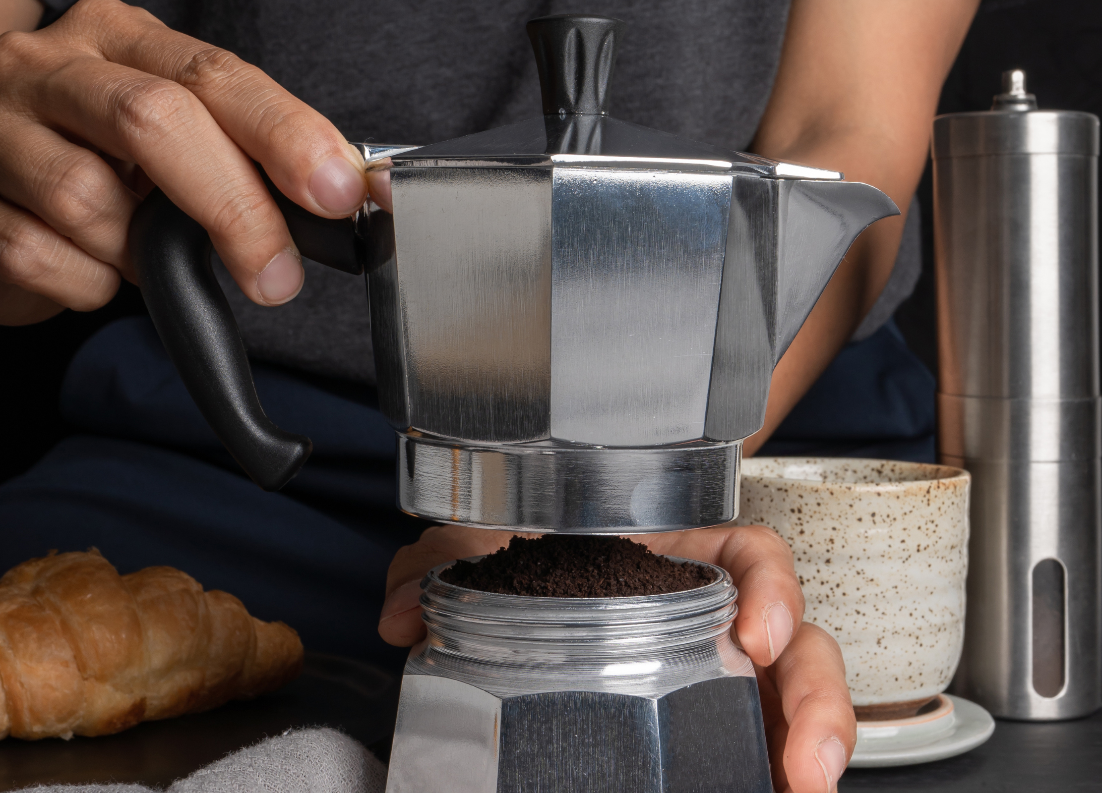 Person schraubt den oberen Teil einer Espressokanne auf den mit Kaffeepulver gefüllten unteren Teil