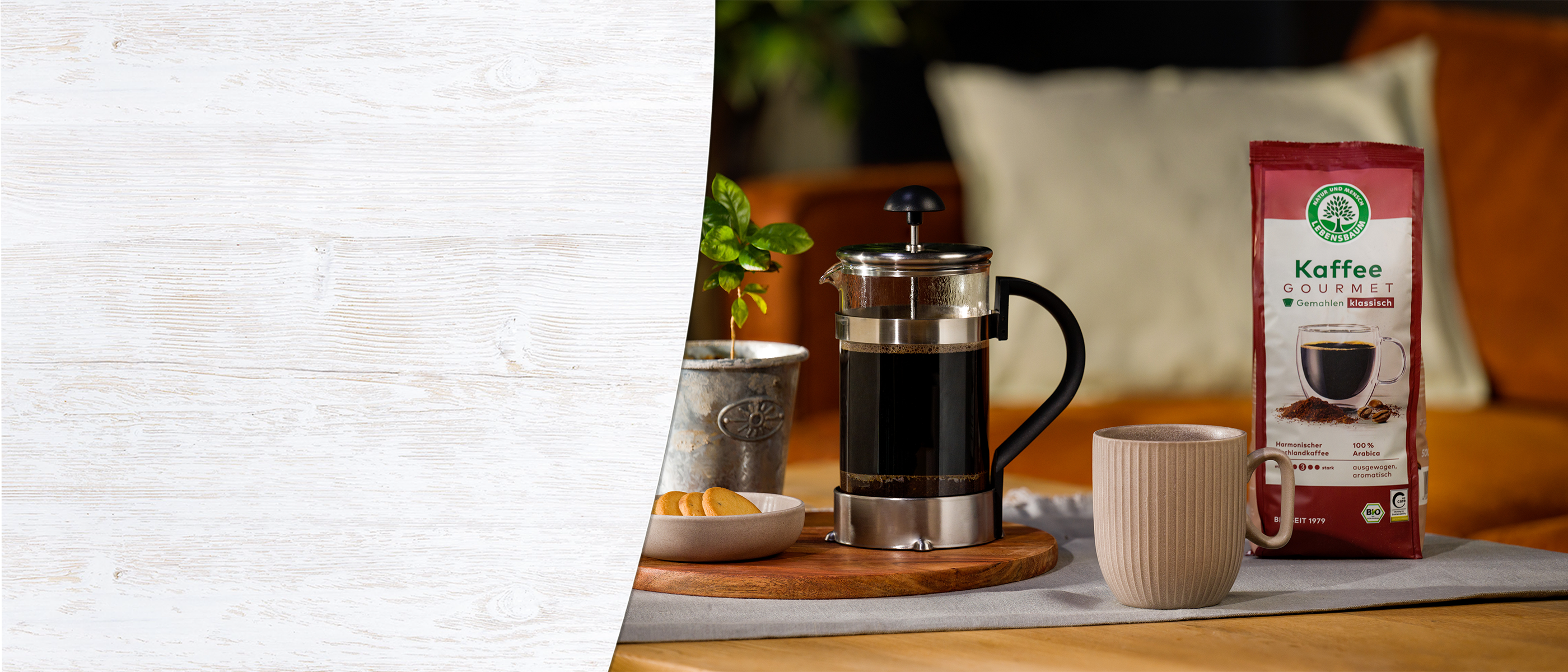 Gourmet Kaffee Lifestyle-Szenerie mit roter Kaffeeverpackung, Stempelkanne und Tasse auf Holzbrett, dekoriert mit Pflanze und Zitrusfrüchten.