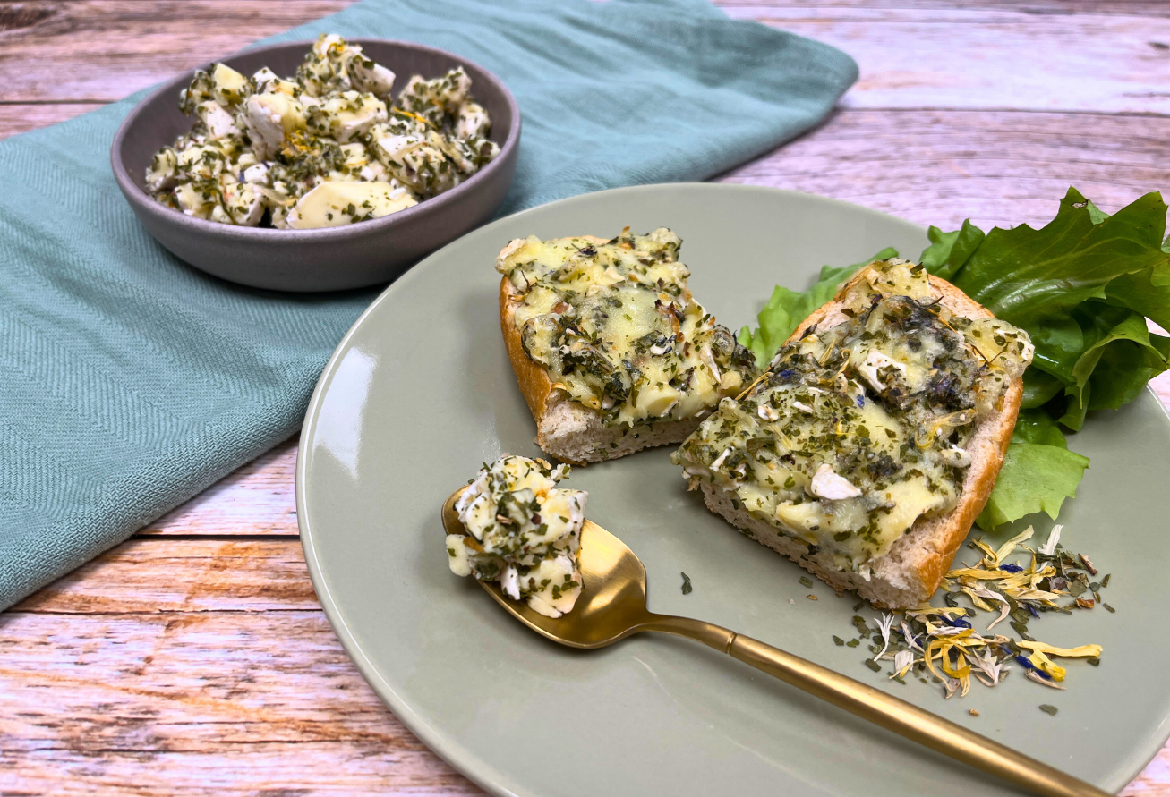 Kräuterbutter auf Brotscheiben mit frischen Kräutern, Salat und goldenem Löffel auf Teller
