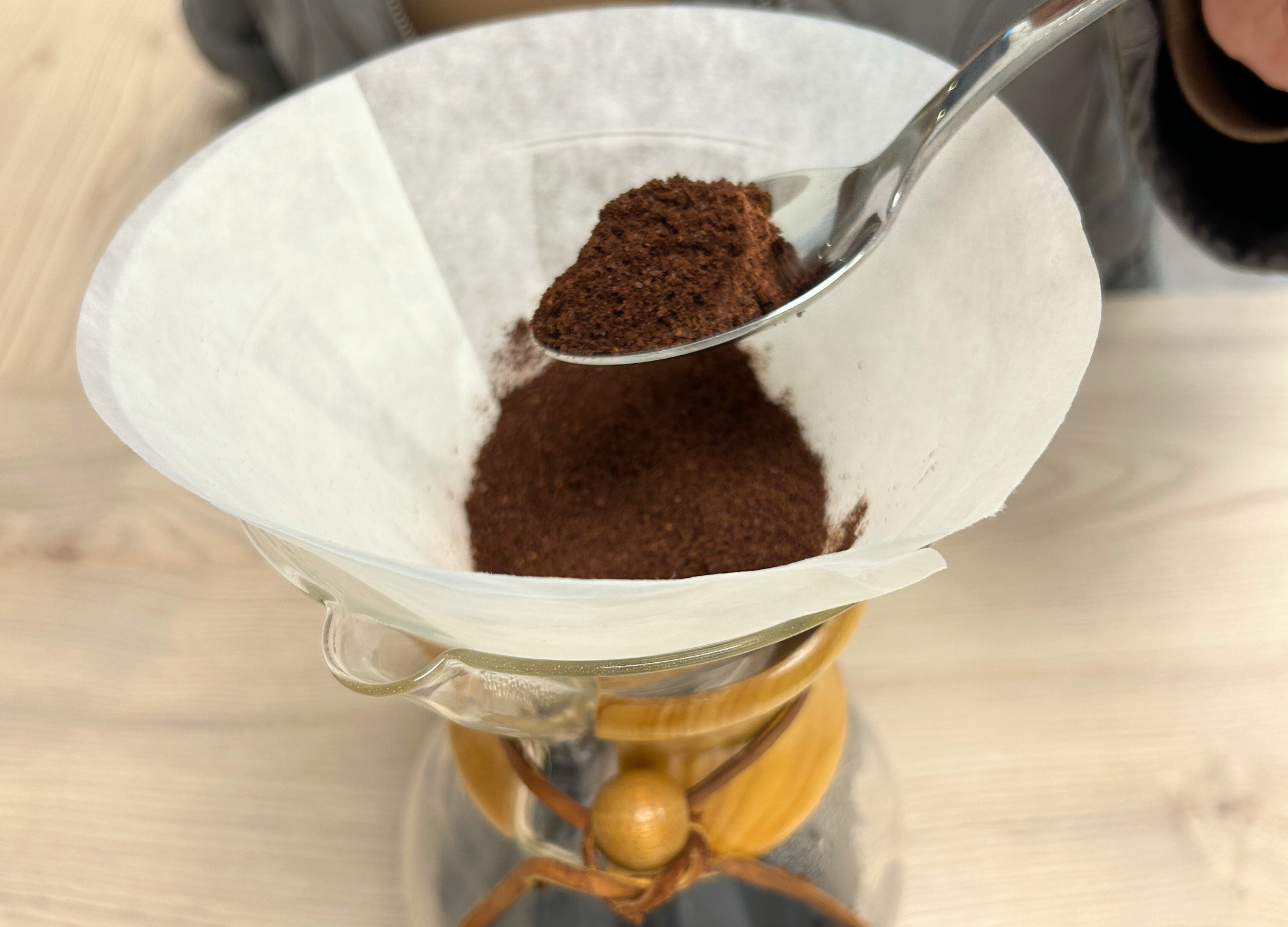 Gemahlener Kaffee wird mit einem Löffel in den Papierfilter einer Chemex-Karaffe gegeben