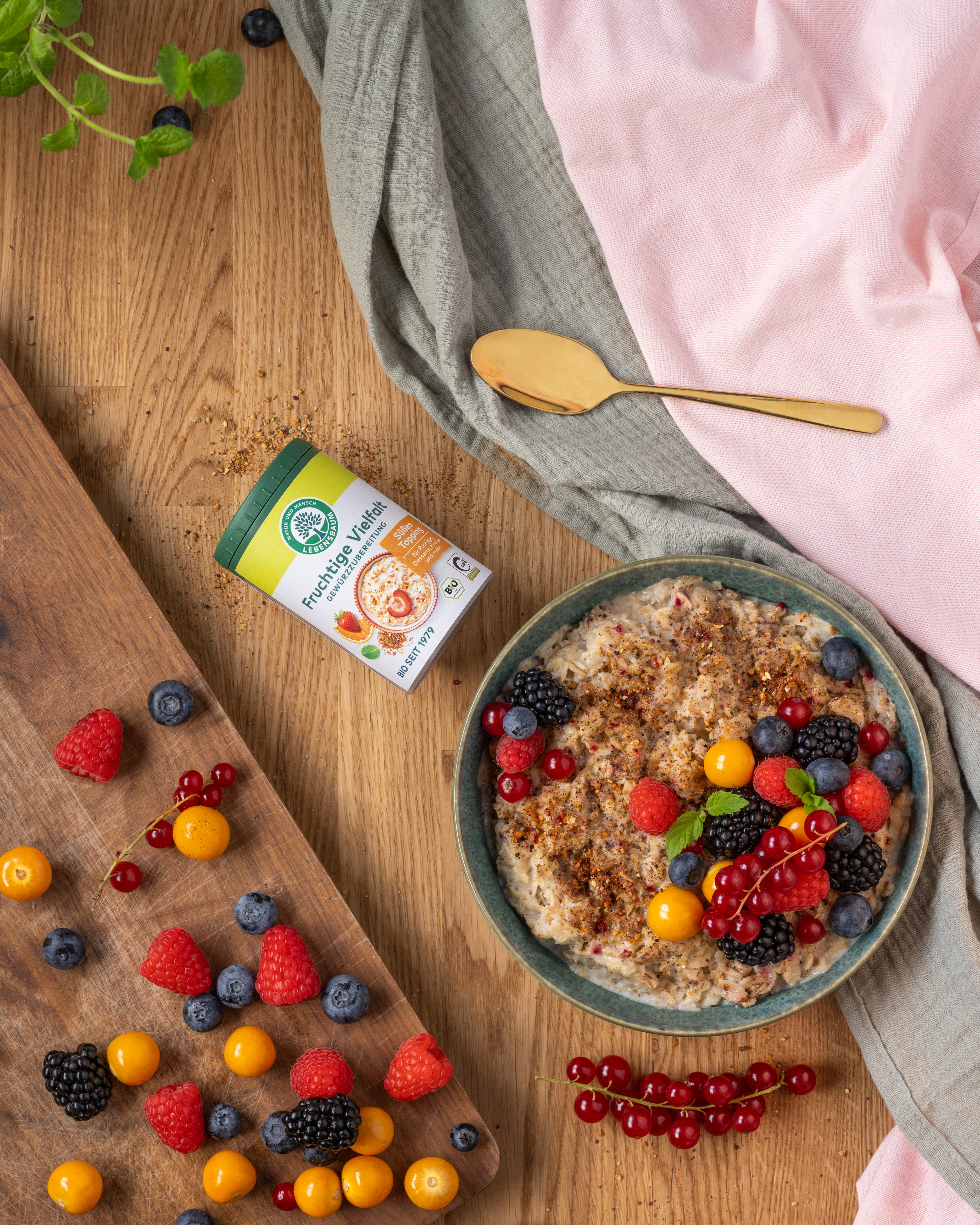Frühstücksmüsli mit Waldbeeren in Schale, daneben Gewürzglas und frische Beeren auf Holzboard