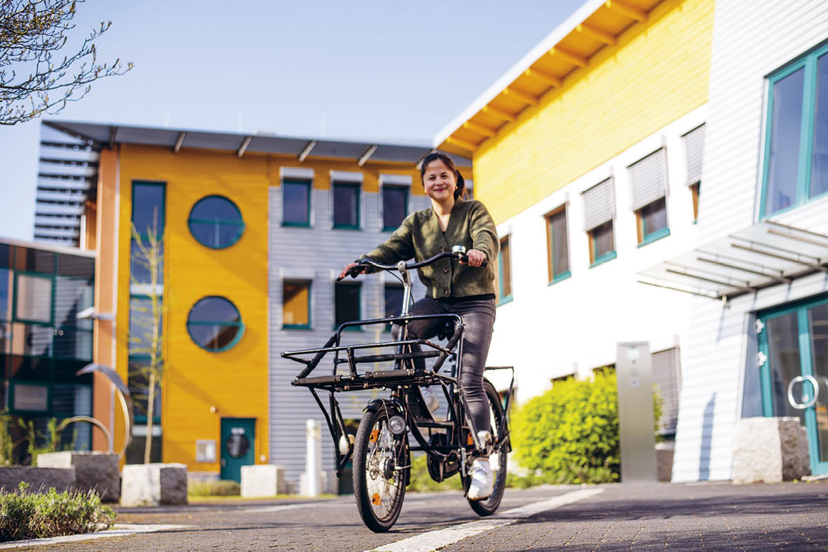 Frau mit Lastenfahrrad vor gelbem und weißem Gebäude in moderner Architektur