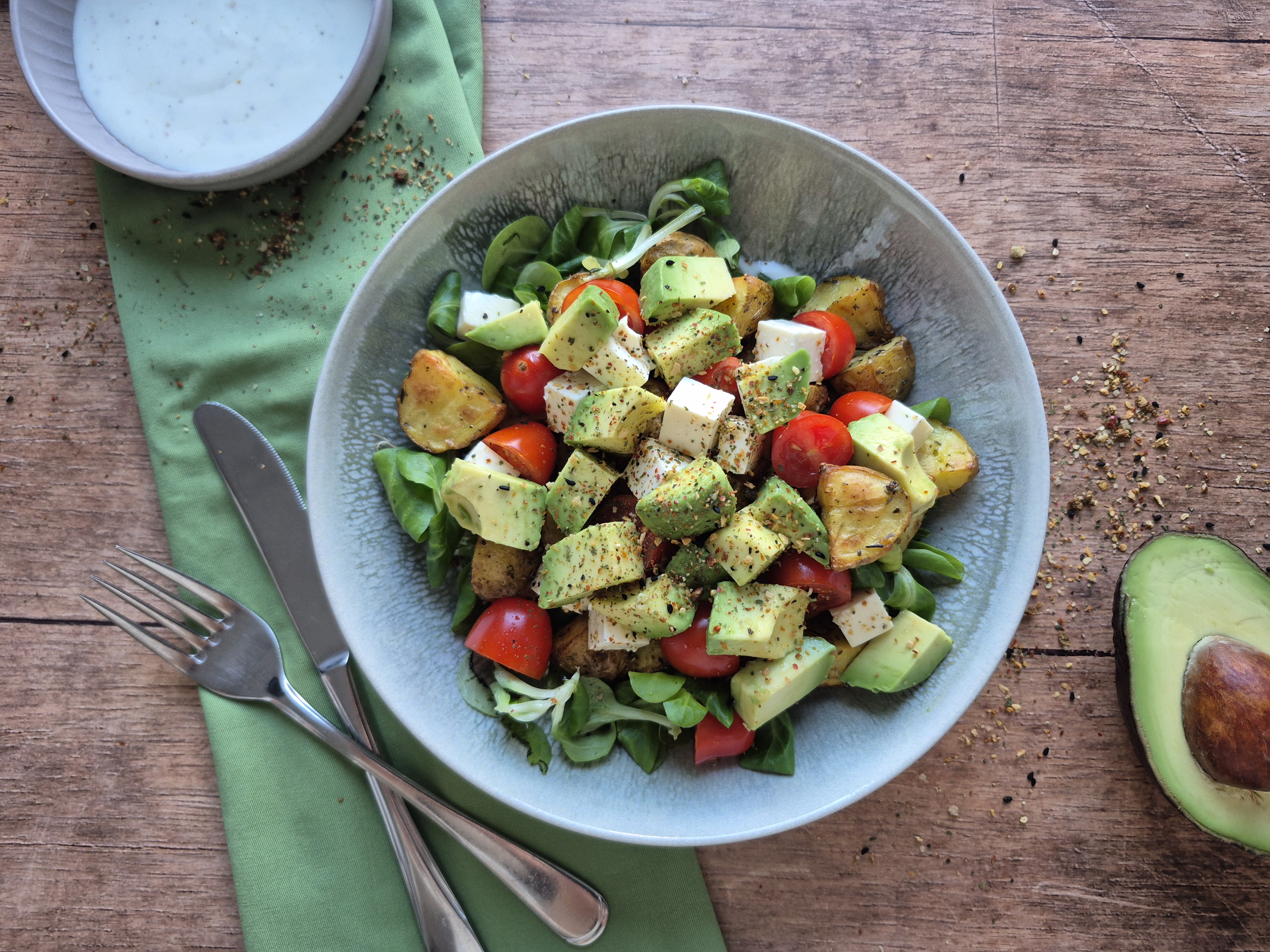 Salat mit Tofu, roten Paprikastreifen, grünen Bohnen und Avocado, gewürzt mit Kräutern, auf Holztisch serviert
